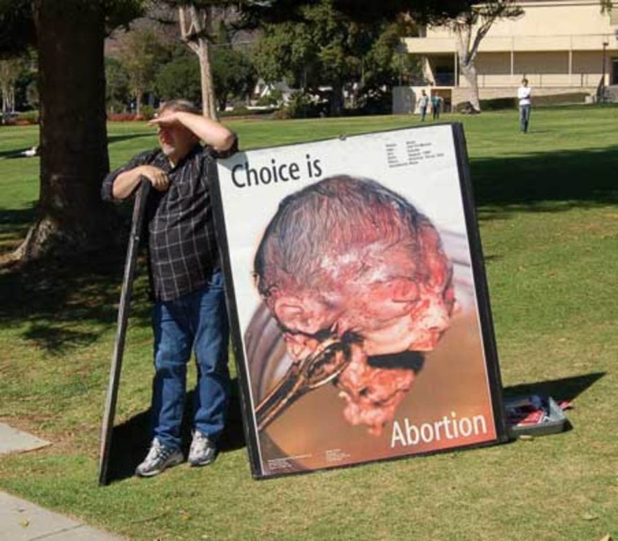 One member of a devout Christian pro-life group who call themselves the "Survivors" stands next to an enlarged photo of an aborted fetus.