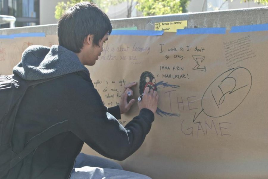 Paul Bacera, 19, Film TV major writes on the writing wall set up along Raider Walk. Its awesome you get to write whatever you want to write or draw, said Bacera.