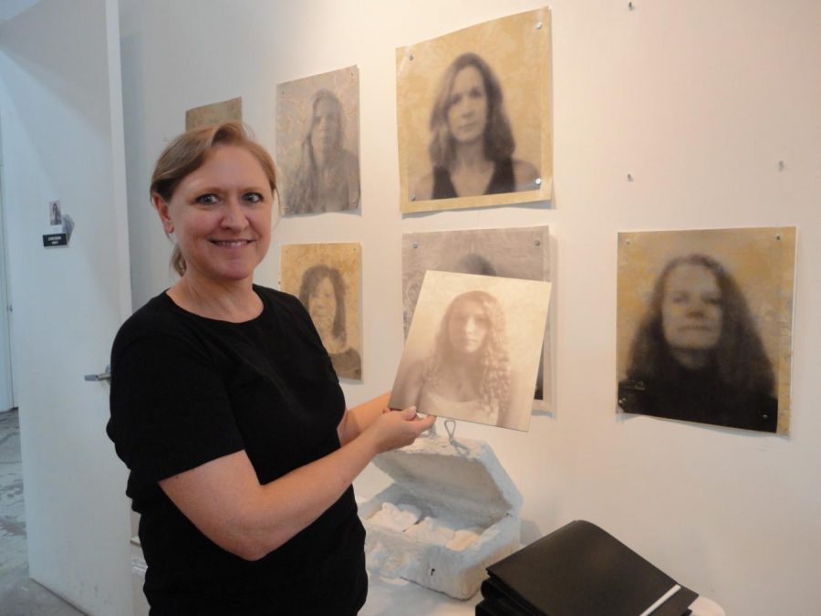 The artist at her studio shows some black and white portraits she made for The Wallflower Project.  Brown printed these portraits directly onto emulsion-covered discontinued wallpaper. Photo credit: Lisette Davies Ward