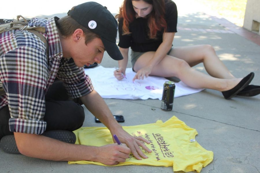 20-year-old Music major Jacob Beeker, left, and 21-year-old Business major Toni Chavez, right, decorate the shirts they intend to hang alongside Raider Walk. The shirts were created as a testimony to the problem of domestic and sexual violence. Photo credit: Nicole Szczepanek