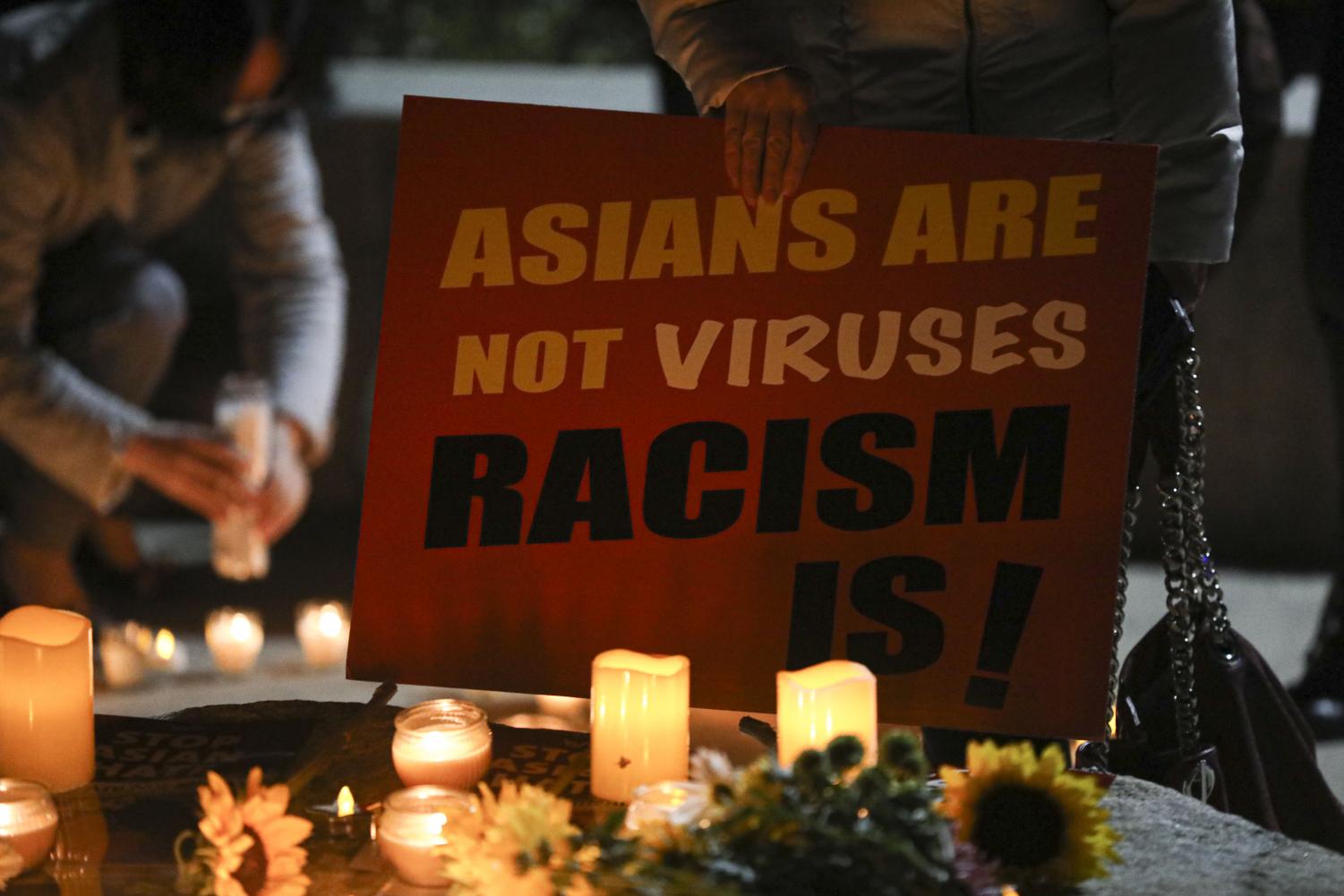 Feng Shen holds up a sign stating "Asians Are not Viruses Racism Is!" in front of candles left out for the eight victims of the Atlanta Mass shooting during the candle light vigil held in Thousand Oaks, CA. on March 20. 2021.