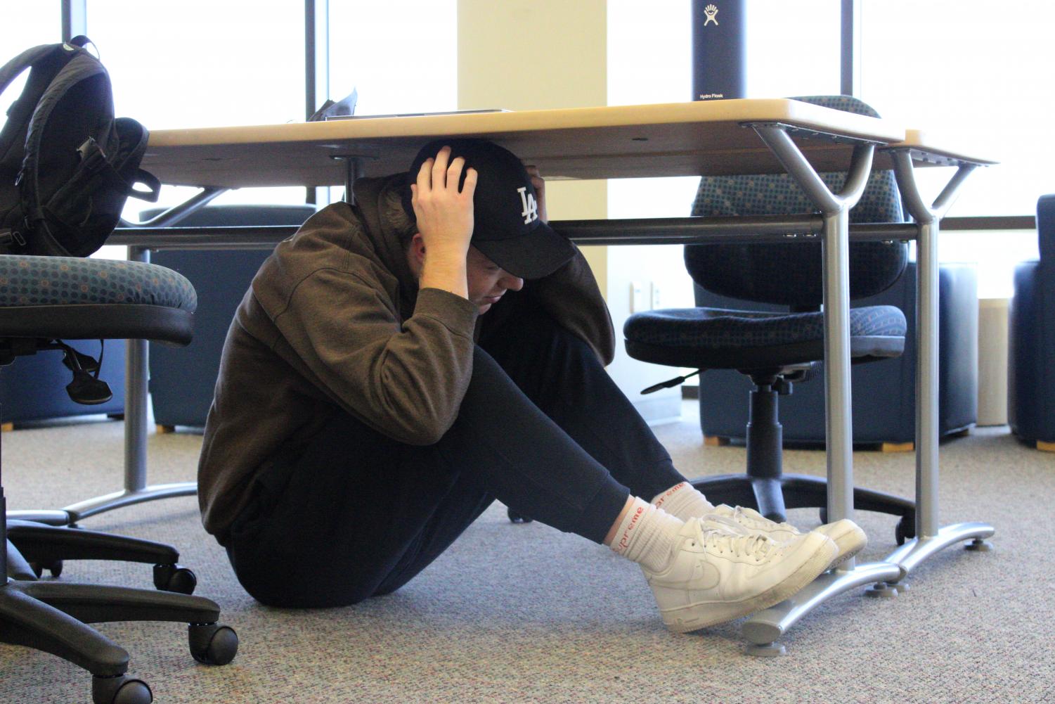 Freshmen Ash Noorzay covers his head as he ducks under a desk in the college library. Immediately following the earthquake drill an evacuation from the building into open space took place.