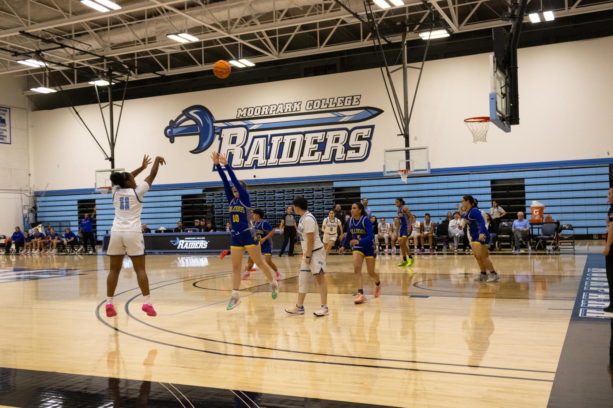 During the Moorpark Community College Women's Basketball game, Moorpark College's Raider Mika Jarrett (left, #11) makes a 3 point shot despite Allan Hancock College's Bulldog Katie Mathews' (#10) attempt to block. Giselle Calderon (#23), Rebecca Saidoff (#21), Makena Melito (#5 Moorpark), Chyanna Tell (#5 Allan Hancok), India Dowling-Green (#1), and Pheobe Becerra (#30) continue the game (from left to right). The Moorpark Raiders played in their home court at Moorpark Community College in Moorpark, CA against Allan Hancock College of Santa Maria, CA on February 14, 2024. Photo by Victoria McLaughlin