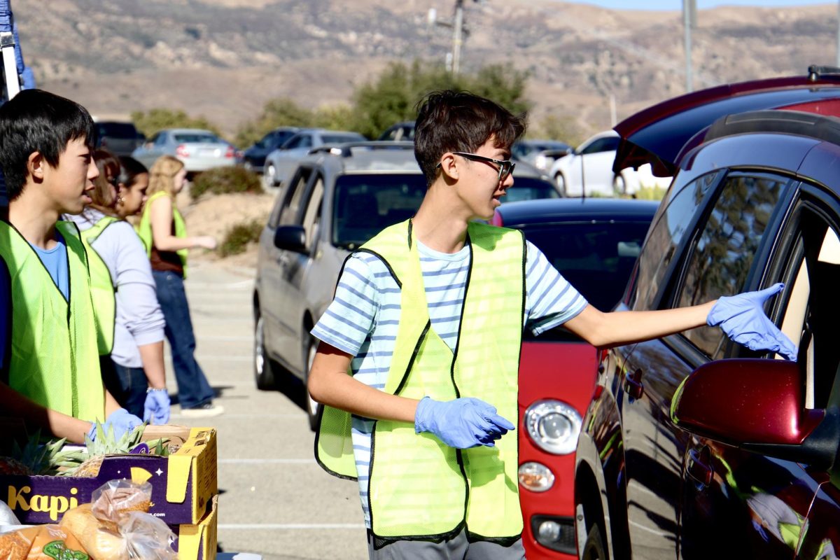 Riley Fong, a student volunteer from Oak Park High School, greets families affected by the Mountain Fire at the emergency food distribution drive-thru on Saturday, Nov. 9 in Moorpark, Calif. Photo credit: Sarah Graue